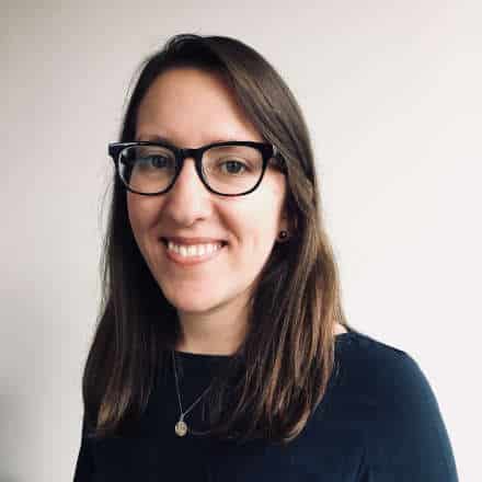 A picture of a woman with brown hair, wearing black glasses, and wearing a black sweater. 