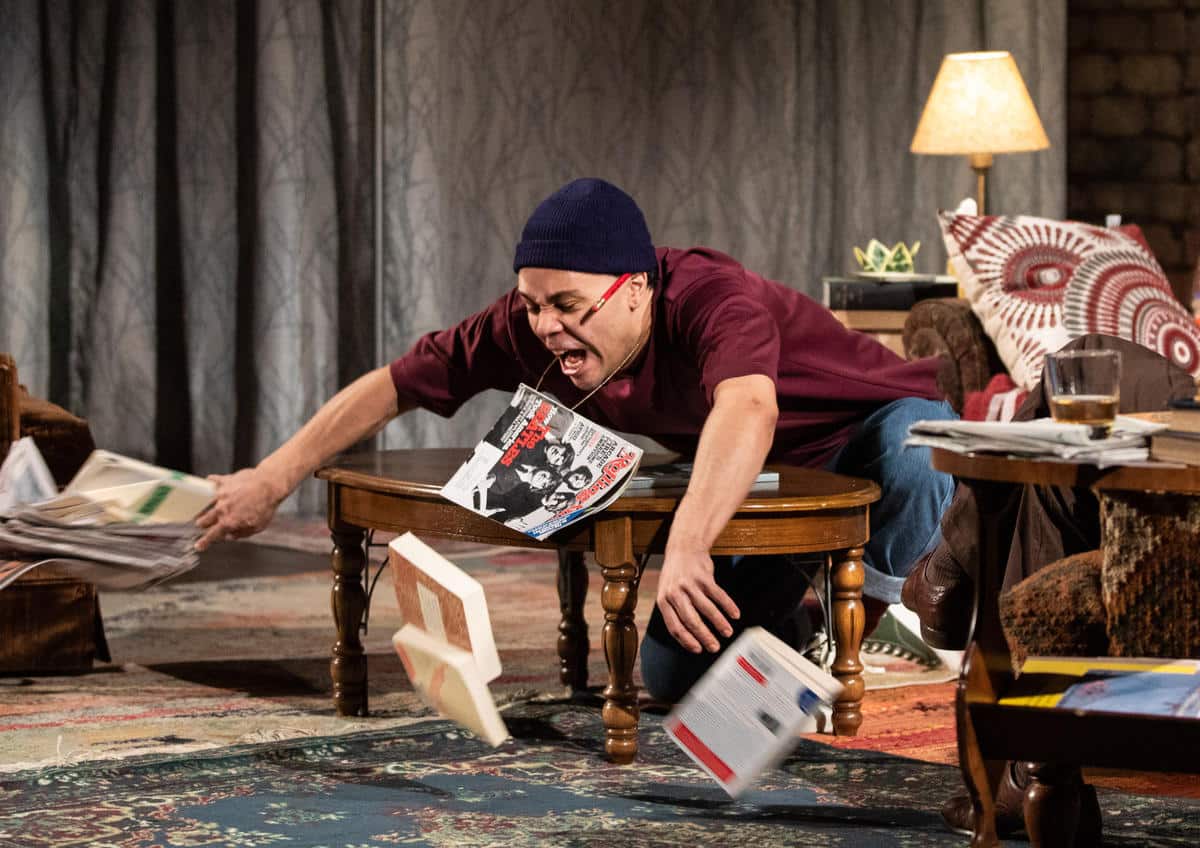 A photo of an actor throwing a bunch of books off a table.