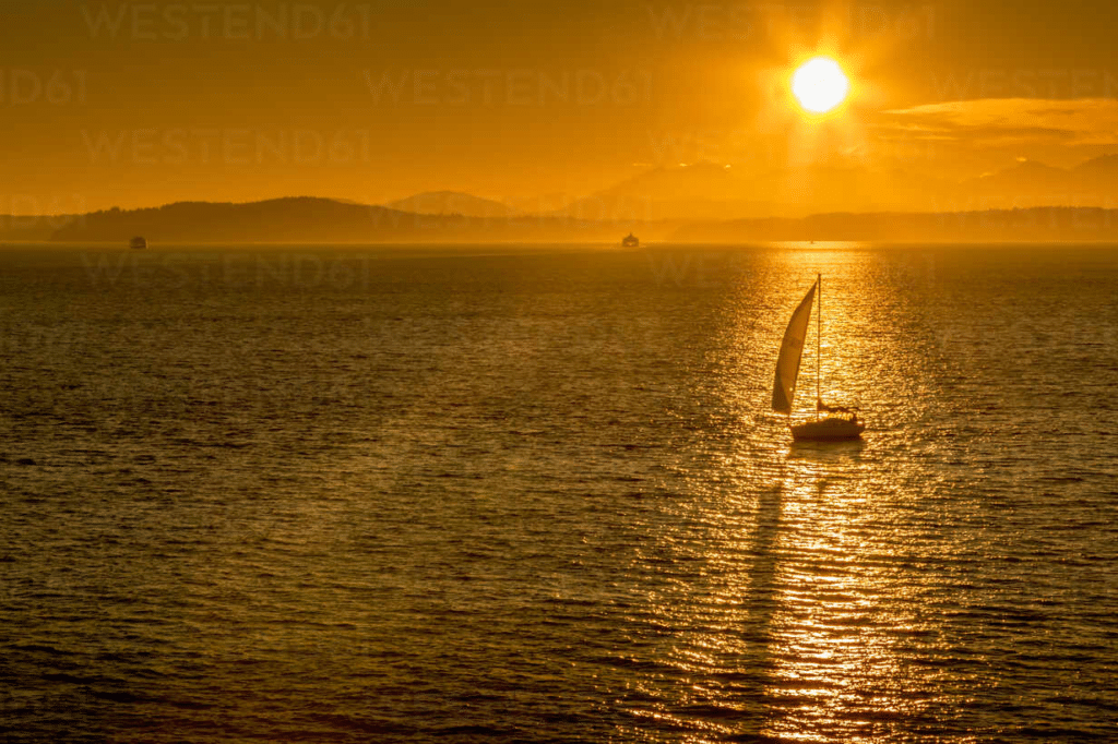 A photo of a sunset over puget sound, with a sailboat. 