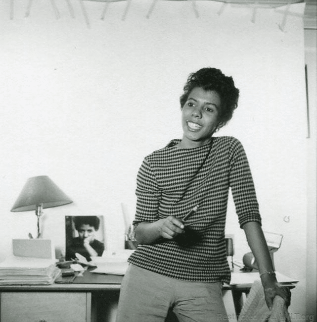 A photo of Lorraine Hansberry in a checked black and white shirt, smiling.