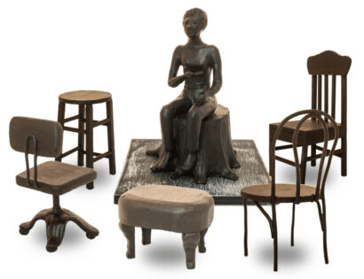 A statue with a chair and a platform with Lorraine Hansberry sitting on it. Around her are five chairs and stools.