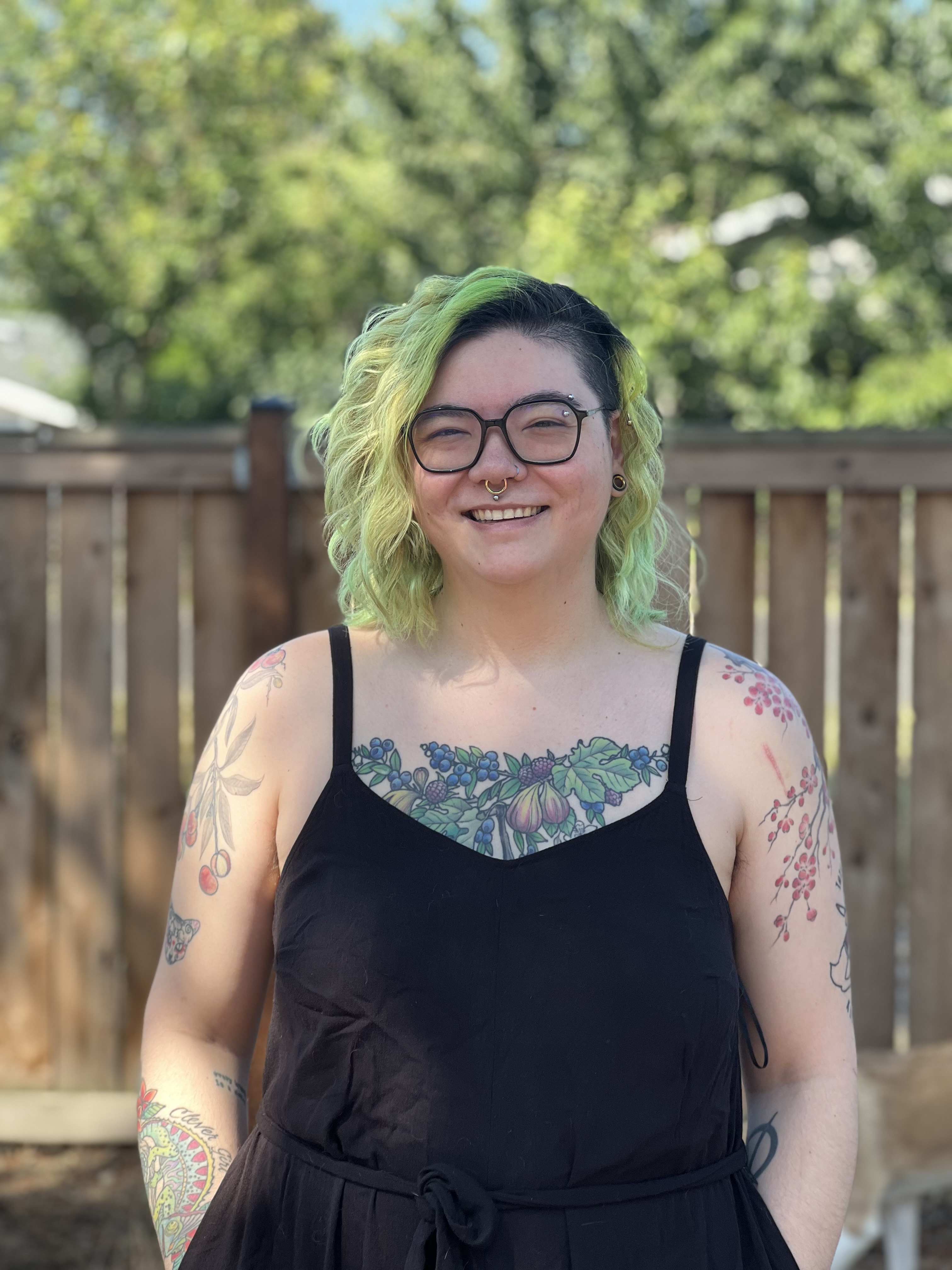 An image of a person with green hair, smiling and wearing a black tank top.